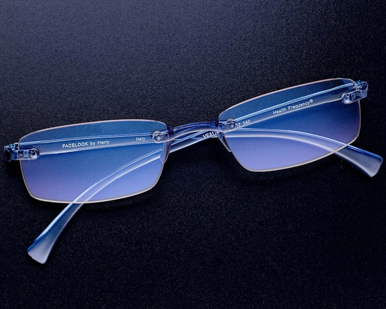 Puede incluir: Gafas azules sin montura con lentes azules degradados. Las gafas tienen el texto "FACELOOK by Harry" e "Italy" impreso en la varilla izquierda y "Health Frequency&reg;" impreso en la varilla derecha.