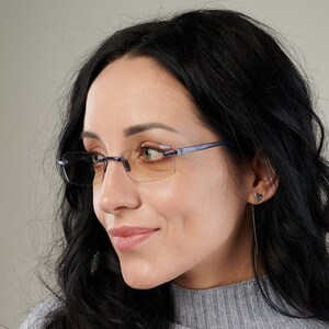 Puede incluir: Una mujer con el pelo largo y negro lleva gafas de montura azul con lentes &aacute;mbar. Las gafas tienen una montura fina y rectangular.