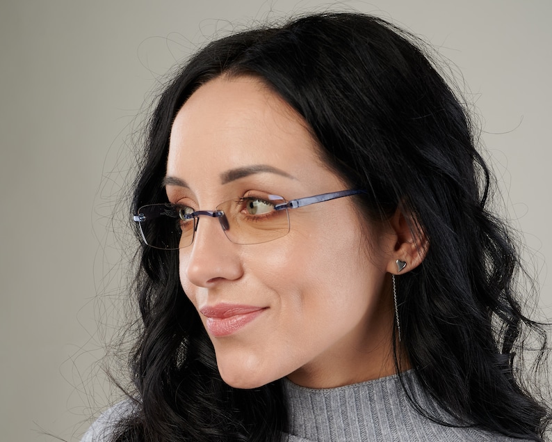 Puede incluir: Una mujer con el pelo largo y negro lleva gafas de montura azul con lentes &aacute;mbar. Las gafas tienen una montura fina y rectangular.
