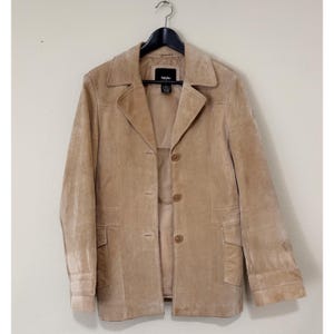 May include: A tan suede jacket with a notched collar, three-button closure, and two front pockets. The jacket is hanging on a black hanger against a neutral background. The brand tag is visible.