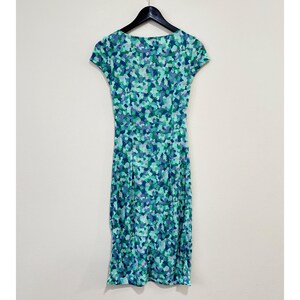 May include: A cap-sleeved dress with a mosaic pattern in blue, green, and purple. The dress hangs on a black hanger against a white background. The dress has a fitted shape. The dress is approximately 100 cm in length.