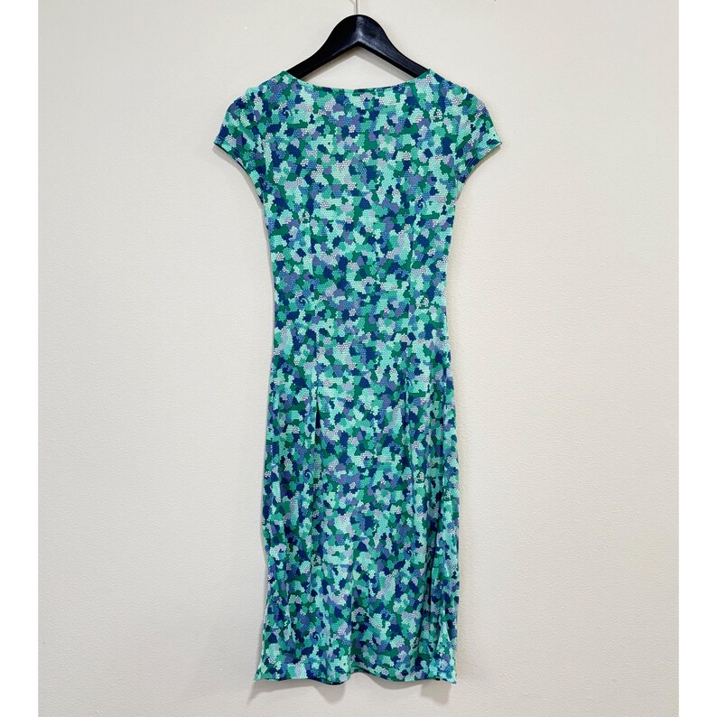 May include: A cap-sleeved dress with a mosaic pattern in blue, green, and purple. The dress hangs on a black hanger against a white background. The dress has a fitted shape. The dress is approximately 100 cm in length.