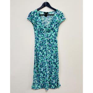 May include: A knee-length dress with a V-neck and short sleeves. The dress features a blue, green, and purple mosaic pattern. The dress is hanging on a black hanger against a white wall.