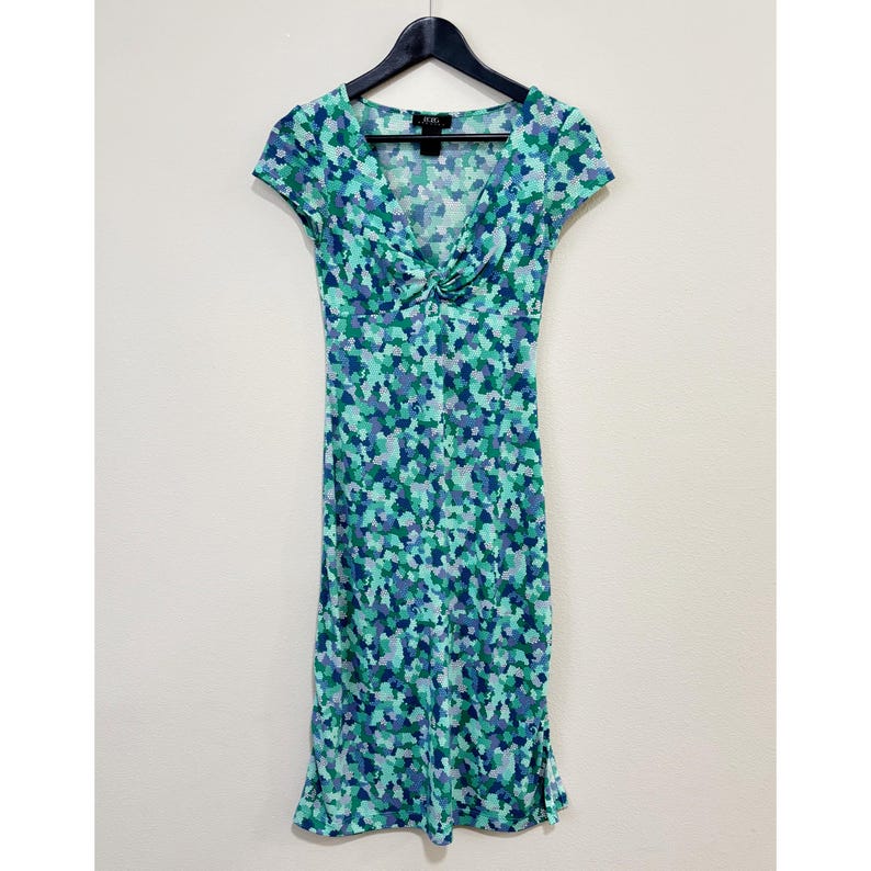 May include: A knee-length dress with a V-neck and short sleeves. The dress features a blue, green, and purple mosaic pattern. The dress is hanging on a black hanger against a white wall.
