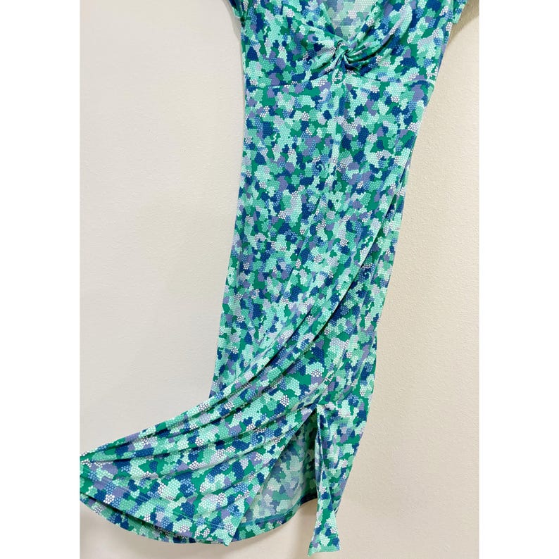 May include: A sleeveless, knee-length dress with a vibrant mosaic pattern in shades of green, blue, and purple. The dress features a knotted detail at the bust and a side slit, creating a flowing silhouette. The fabric appears lightweight and suitable for warm weather.