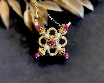 May include: A gold-toned necklace featuring a floral pendant with a central cluster of white pearls and surrounding red gemstones. The pendant is intricately designed with a delicate chain and is set against a dark background.