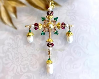 May include: A gold-toned pendant necklace and earrings set. The cross-shaped pendant features red, green, and white accents, with a central pearl and dangling pearl drops. The earrings mirror the pendant's design, with pearl drops and gold-toned caps.