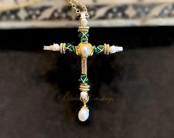 May include: A gold-colored cross pendant necklace with a delicate chain. The cross features a central pearl, green beads, and smaller pearls. The design includes intricate wire wrapping and the text "Divine Crossings".