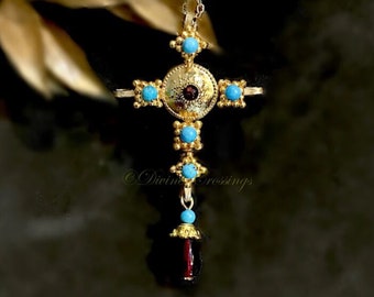 May include: A gold-colored pendant necklace featuring a cross design. The cross is adorned with turquoise-colored stones and a central circular element with a dark red stone. The pendant hangs from a delicate silver chain.