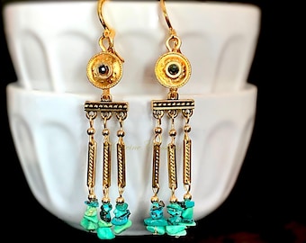 May include: A pair of gold-toned dangle earrings featuring a circular stud with a dark center stone, a horizontal bar, and three hanging chains. Each chain ends with a cluster of small, irregular, bright turquoise-colored stone chips.