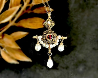 May include: A gold-toned pendant necklace featuring an ornate metal centerpiece with a central dark red gemstone. The design is accented with small white pearls arranged in a semi-circle and three dangling teardrop-shaped white pearls.