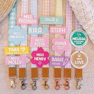 Può includere: Una collezione di cordini in tessuto con motivi a quadretti vichy pastello in blu, rosa, arancione, giallo e viola. Ogni cordino include una targhetta personalizzata in acrilico con nomi in varie forme come fiori, rettangoli e cerchi.