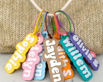 May include: A set of seven colorful personalized keychains with names "Sophie", "Evelyn", "Willow", "Faith", "Jayden", "William", and "Olivia" written in a bubbly font.