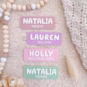 May include: Four pastel-coloured name badges. Each badge displays a name and title in white, 3D lettering. The names are Natalia, Lauren, and Holly. Titles include Midwife, Educator, and Registered Nurse. The badges are pink, lavender, and green.