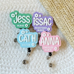 A selection of colourful name badge reel with flowers, each displaying a name and profession. Examples include "Jess, Nurse". The tags are in shades of pink, blue, green, yellow, and purple, with white text.