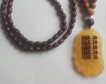 May include: A brown wooden beaded necklace with a yellow abacus pendant. The abacus has brown beads and a black bead at the top.