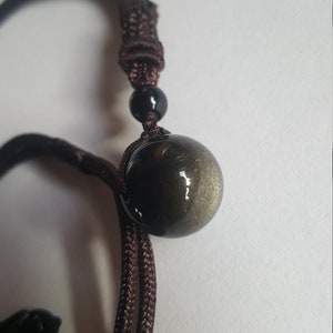 May include: A brown cord necklace with a gold and black round gemstone pendant.