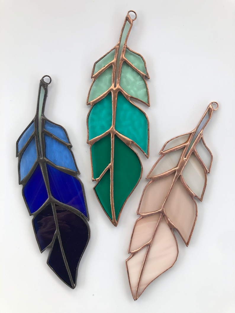 May include: Three stained glass feathers, one blue, one green, and one pink, with copper wire accents.
