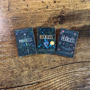 Pode incluir: Tr&ecirc;s livros de bolso com capas pretas e desenhos florais. Os t&iacute;tulos s&atilde;o "Powerless", "Reckless" e "Fearless" de Lauren Roberts.