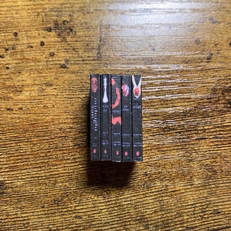 May include: A set of five paperback books with black covers and red and white text. The titles of the books are "Twilight", "New Moon", "Eclipse", "Breaking Dawn", and "Midnight Sun".