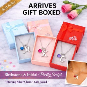 Peut inclure: Colliers avec initiales et pierres de naissance présentés dans des coffrets cadeaux. Chaque collier comprend une chaîne en argent, un pendentif lettre et une pierre précieuse colorée. Les boîtes sont de couleurs variées. Le texte "ARRIVES GIFT BOXED" est visible.