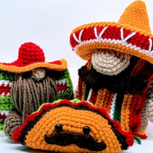 May include: Two crocheted gnomes wearing traditional Mexican sombreros, one holding a crocheted taco with a mustache and googly eyes.