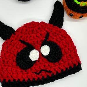 Peut inclure: Un bonnet de diable crocheté rouge et noir avec de grands yeux noirs, des reflets blancs et des cornes noires. Le chapeau a un bord noir et est probablement fait à la main. Cet article convient à Halloween ou aux soirées costumées.