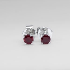 May include: A pair of stud earrings with round, deep red gemstones set in silver-coloured metal. The earrings have a classic design, with the gemstones held by small prongs. The posts and backs are also silver-toned.
