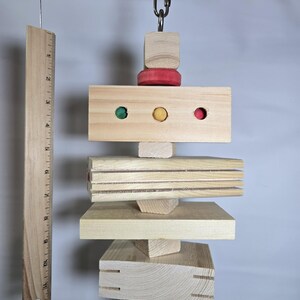Puede incluir: Un juguete de madera para p&aacute;jaros con varias formas y colores. El juguete est&aacute; suspendido de una rama y presenta una regla para la comparaci&oacute;n de tama&ntilde;os. El juguete incluye detalles en rojo, verde y amarillo.