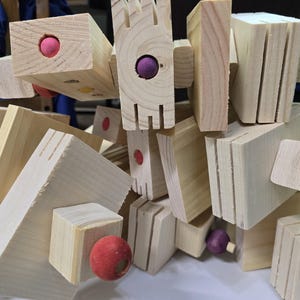 Puede incluir: Primer plano de un juego de construcci&oacute;n de madera. El conjunto presenta varias formas geom&eacute;tricas, incluyendo bloques y tablones, conectados con peque&ntilde;as esferas de colores. La veta natural de la madera es visible, y las piezas est&aacute;n dispuestas en una pila aparentemente aleatoria.
