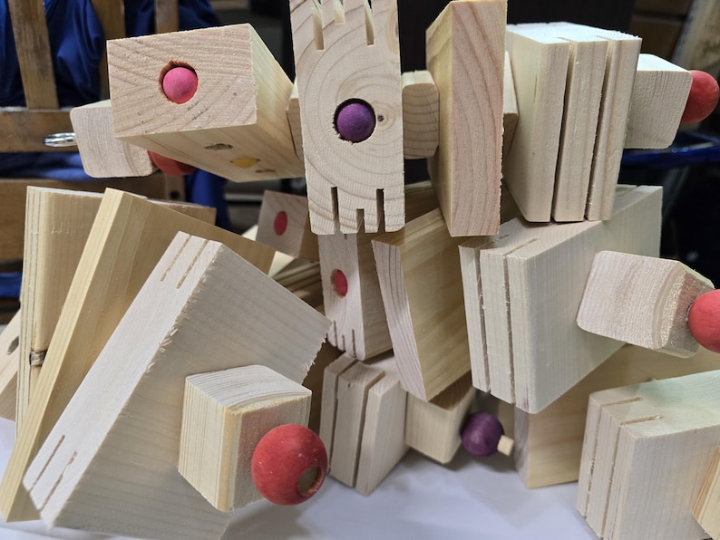 Puede incluir: Primer plano de un juego de construcci&oacute;n de madera. El conjunto presenta varias formas geom&eacute;tricas, incluyendo bloques y tablones, conectados con peque&ntilde;as esferas de colores. La veta natural de la madera es visible, y las piezas est&aacute;n dispuestas en una pila aparentemente aleatoria.
