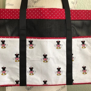 May include: Red and white polka dot tote bag with black straps and a black mesh panel. The bag features a white background with a repeating pattern of Minnie Mouse.