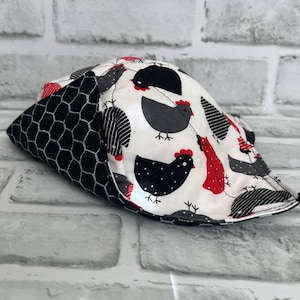May include: A white fabric hat with a black and white chicken pattern and red accents. The hat has a black and white checkered fabric lining.