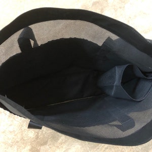 May include: Black mesh tote bag with a zippered pocket on the inside. The bag has a black fabric lining and a black handle.