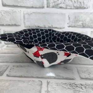 May include: A black and white fabric bowl with a honeycomb pattern on the outside and a white fabric lining with a red and black chicken pattern on the inside.