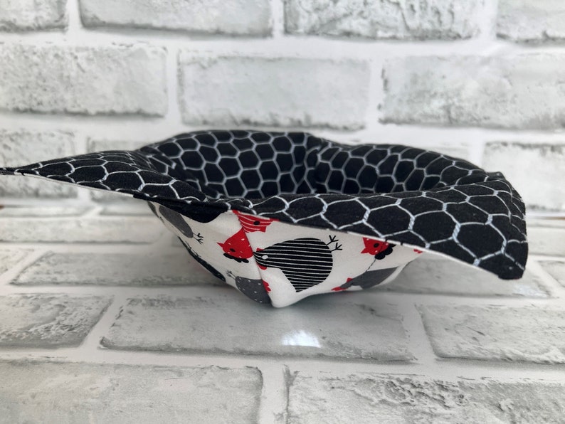 May include: A black and white fabric bowl with a honeycomb pattern on the outside and a white fabric lining with a red and black chicken pattern on the inside.