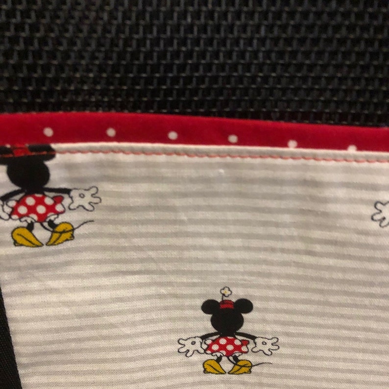 May include: A white fabric with gray stripes and red polka dots. Two black and white Mickey Mouse figures are printed on the fabric. The fabric has a red border with white polka dots.