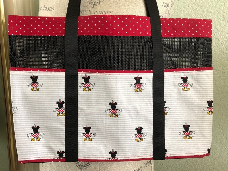 May include: Red and white polka dot tote bag with black straps and a black mesh panel. The bag features a white background with a repeating pattern of Minnie Mouse.