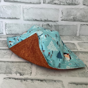 May include: A blue and brown fabric bowl with a wintery pattern of trees, snowflakes, and animals. The bowl is folded up and has a brown fabric lining.