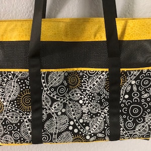 May include: A black and white tote bag with a yellow trim and black straps. The bag features an Aboriginal-inspired design with white dots, lines, and swirls on a black background.