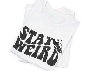 May include: White t-shirt with black text that says "Stay Weird" and a black UFO graphic.