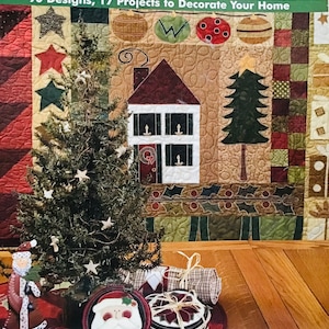 Puede incluir: Un libro titulado "A Cozy Quilted Christmas" con un diseño acolchado rojo, verde y marrón que presenta una casa, un árbol de Navidad y adornos. La portada del libro también incluye el texto "90 Designs, 17 Projects to Decorate Your Home".