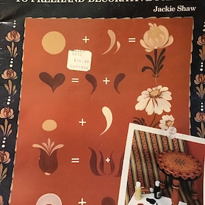 May include: A book titled "Beginner's Guide to Freehand Decorative Painting" by Jackie Shaw. The cover features a red background with illustrations of various floral and geometric shapes. The book includes instructions on how to create these designs using freehand techniques.