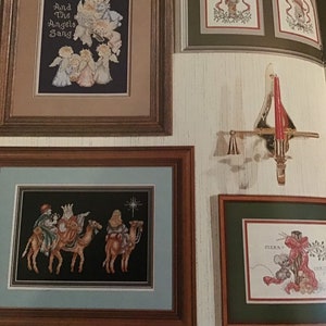 Puede incluir: Cuatro piezas de bordado de punto de cruz enmarcadas con un tema navide&ntilde;o. La pieza superior izquierda presenta &aacute;ngeles cantando con el texto "And The Angels Sang". La pieza superior derecha presenta un ni&ntilde;o peque&ntilde;o con un gorro rojo y un abrigo verde de pie en una puerta con un lazo rojo. La pieza inferior izquierda presenta a los tres reyes magos montando camellos con una estrella en el cielo. La pieza inferior derecha presenta un rat&oacute;n sosteniendo un lazo rojo con el texto "Merry Christmas".