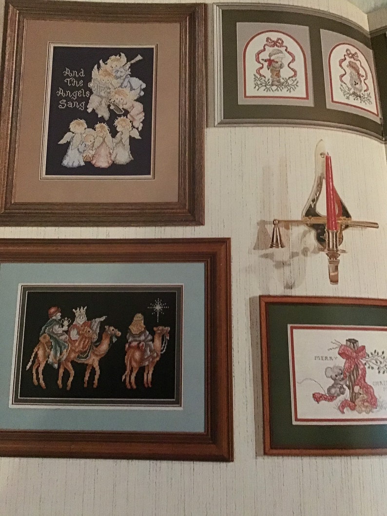 Puede incluir: Cuatro piezas de bordado de punto de cruz enmarcadas con un tema navide&ntilde;o. La pieza superior izquierda presenta &aacute;ngeles cantando con el texto "And The Angels Sang". La pieza superior derecha presenta un ni&ntilde;o peque&ntilde;o con un gorro rojo y un abrigo verde de pie en una puerta con un lazo rojo. La pieza inferior izquierda presenta a los tres reyes magos montando camellos con una estrella en el cielo. La pieza inferior derecha presenta un rat&oacute;n sosteniendo un lazo rojo con el texto "Merry Christmas".