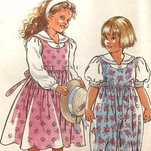 Puede incluir: Un patrón de costura para dos vestidos de niños. El patrón es para las tallas 3-8 e incluye un vestido floral rosa con una blusa blanca y un mono floral azul. El patrón se titula "It's So Easy It's Simplicity" y el número de patrón es 7417.
