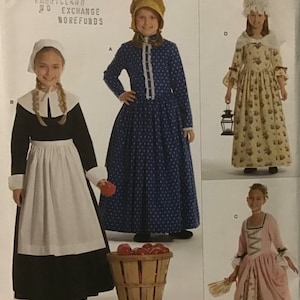 May include: A sewing pattern for three different children's dresses. The pattern is for sizes K5, 7, 8, 10, 12, and 14. The dresses are all different styles, one is a blue dress with white polka dots, one is a pink dress with a floral print, and one is a black dress with a white apron. The pattern is from Simplicity and is number 3725.