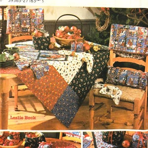May include: A Christmas table setting featuring a red, white and blue patchwork tablecloth, a basket of baubles, and a chair with a Christmas-themed cushion. The table setting includes placemats, napkins and a napkin ring. The image also shows a close-up of a Christmas-themed placemat with a Santa Claus design.