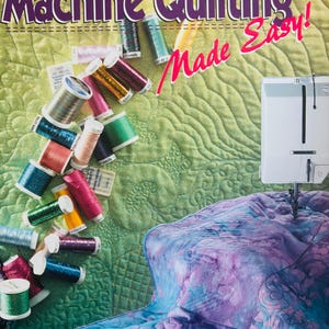 Puede incluir: Portada del libro "Machine Quilting Made Easy!" con una máquina de coser y coloridas bobinas de hilo. El fondo es una tela acolchada en tonos verdes y morados. El nombre de la autora, Maurine Noble, está en la parte inferior.