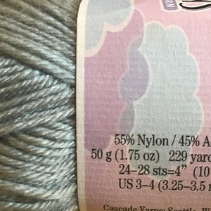 Op de afbeelding: Een bol lichtgrijs garen met een label met de tekst "55% Nylon / 45% Acryl 50 g (1,75 oz) 229 yards (210 24-28 st=4" (10 cm) US 3-4 (3,25-3,5 mm)"
